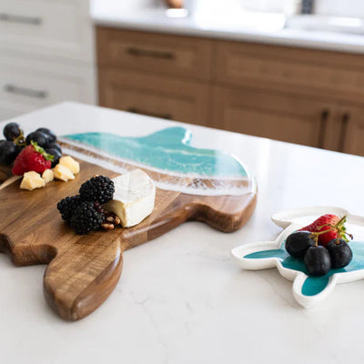 Handcrafted sea turtle-shaped charcuterie board with acacia wood and blue resin accents, topped with fruit and cheese.