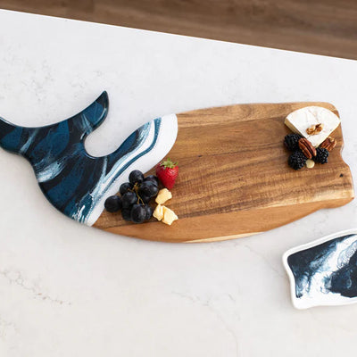 Wooden whale-shaped charcuterie board with ocean-inspired resin design on a white surface