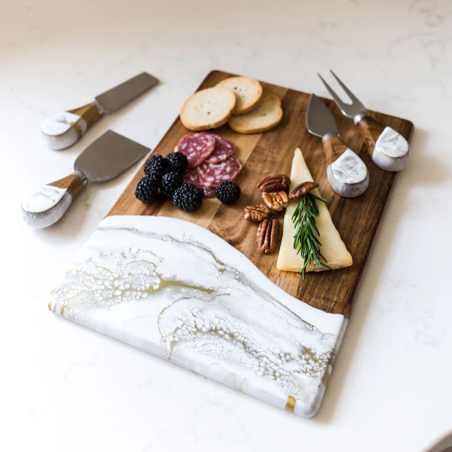 Wooden charcuterie board with assorted cheeses, fruits, and accompaniments on a marble surface.