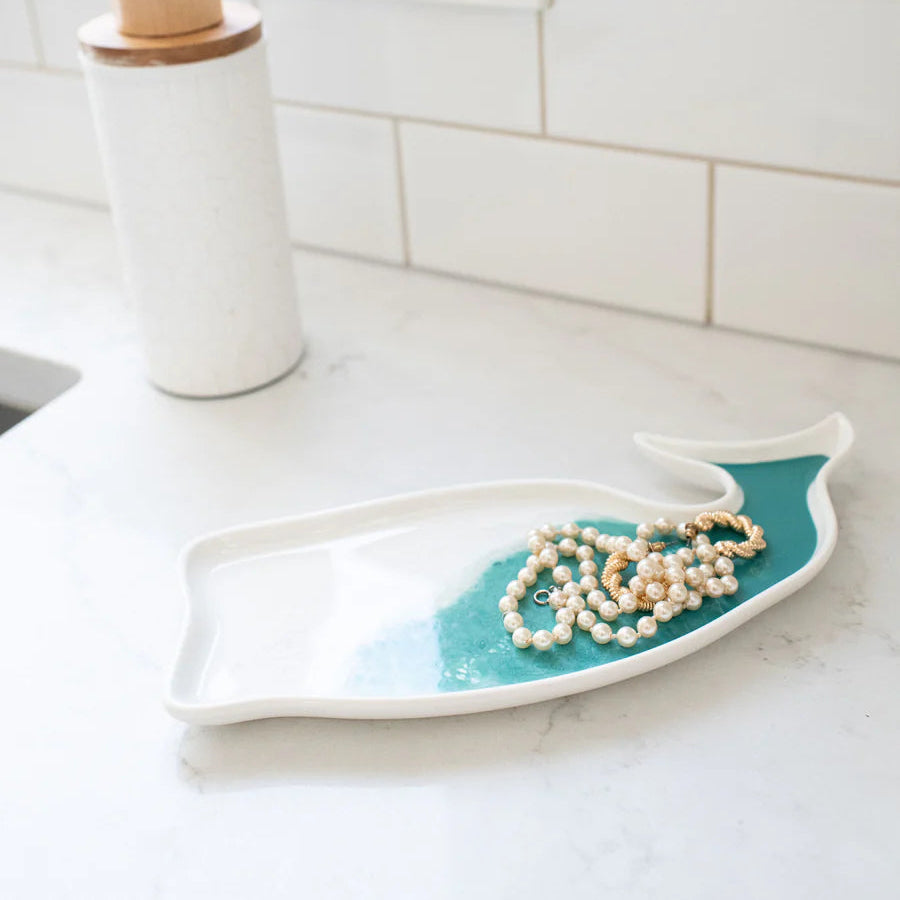White and turquoise resin whale shaped tray with pearls on a white tiled bathroom counter.