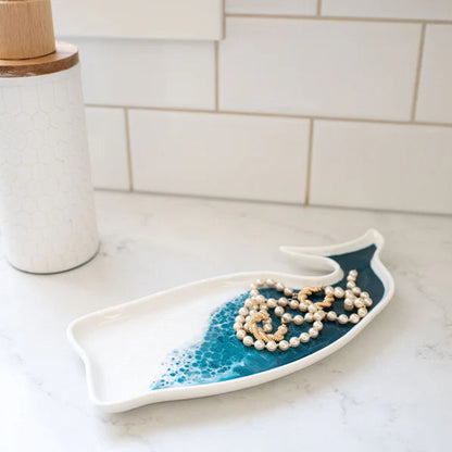 Decorative resin ceramic dish shaped like a wave on a kitchen counter with a necklace on it.