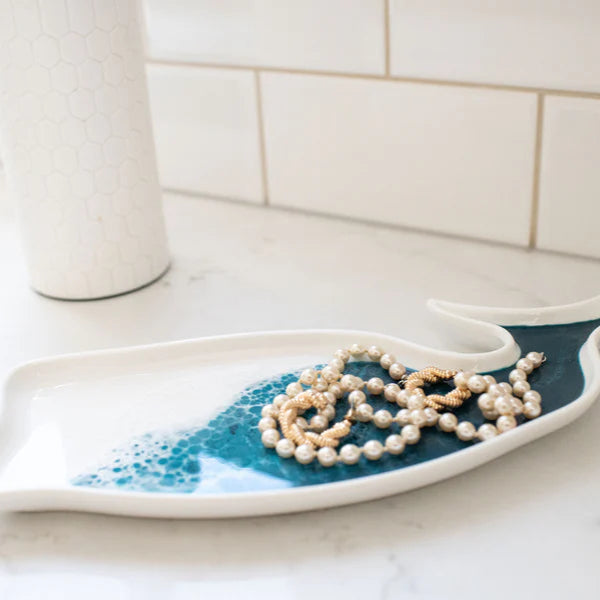 Decorative resin tray with blue wave design holding a necklace on a white surface.