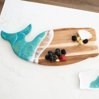 Wooden whale-shaped charcuterie board with ocean-inspired resin design on a white surface