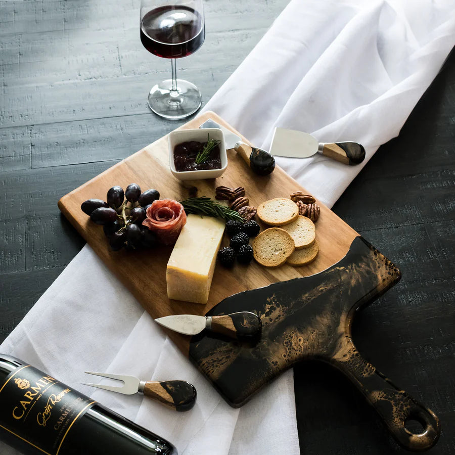 Wooden charcuterie board with cheese, fruits, and a bottle of wine on a white cloth.