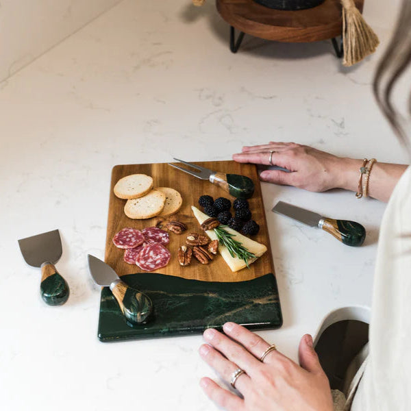 Person preparing a charcuterie board with various meats and cheeses on a marble countertop.