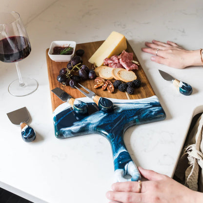 Marble-patterned resin cheese knife on a cutting board with food and wine.