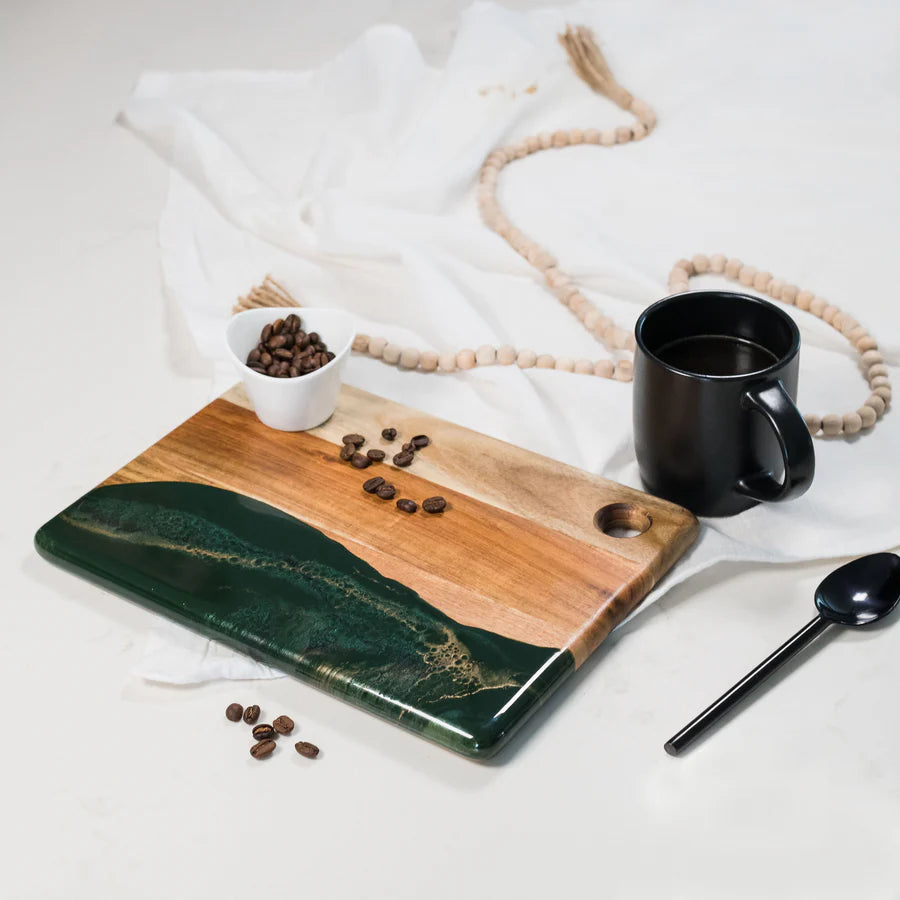 Wooden Cheese Charcuterie Serving Board with green resin finish, black mug, and coffee beans on a white surface.