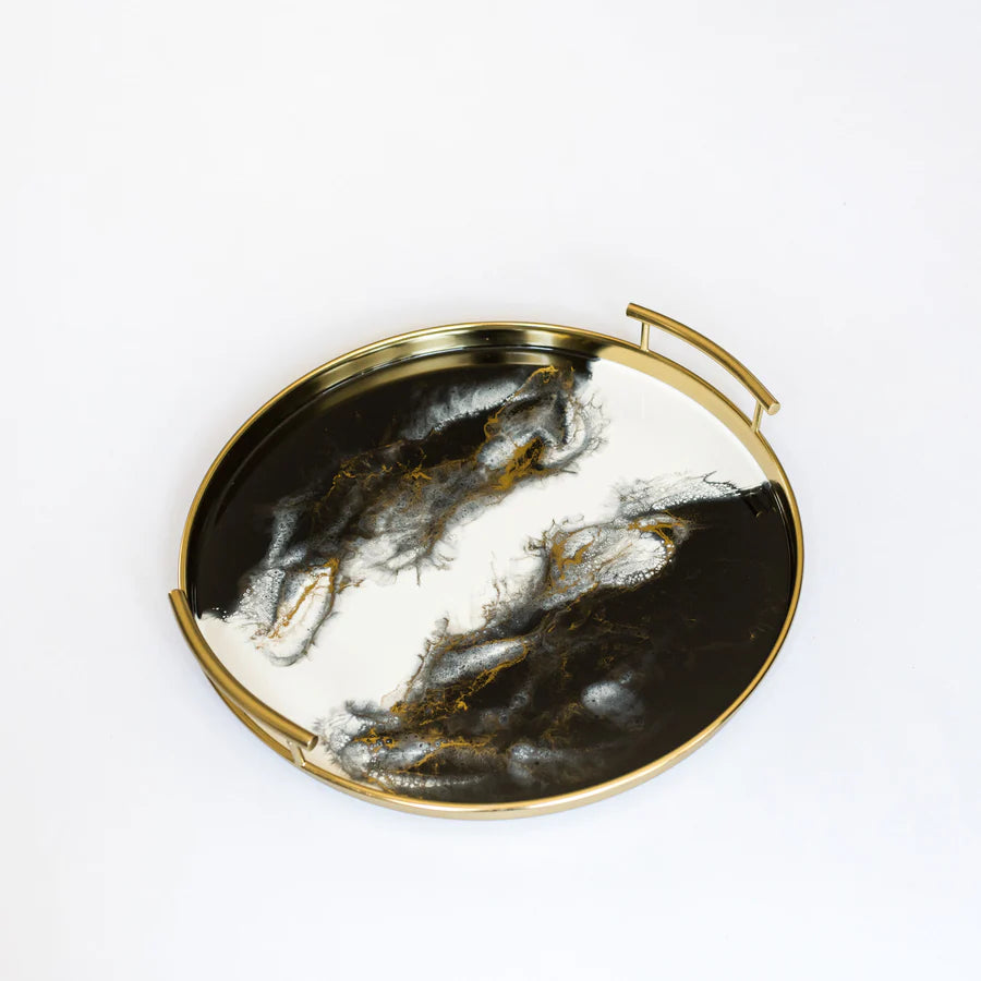 Round decorative tray with gold rim and black and white resin marbled design on a white background