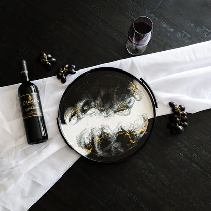 Decorative resin tray with artistic design, wine bottle, and glass on a black surface.