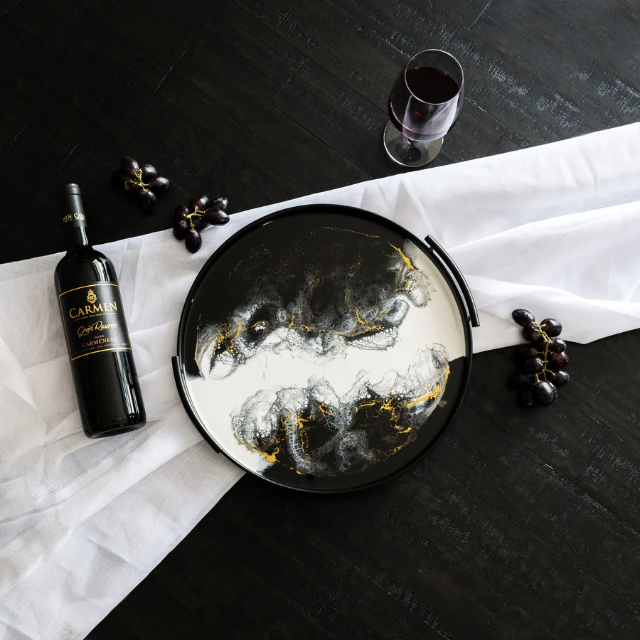 Decorative resin tray with artistic design, wine bottle, and glass on a black surface.