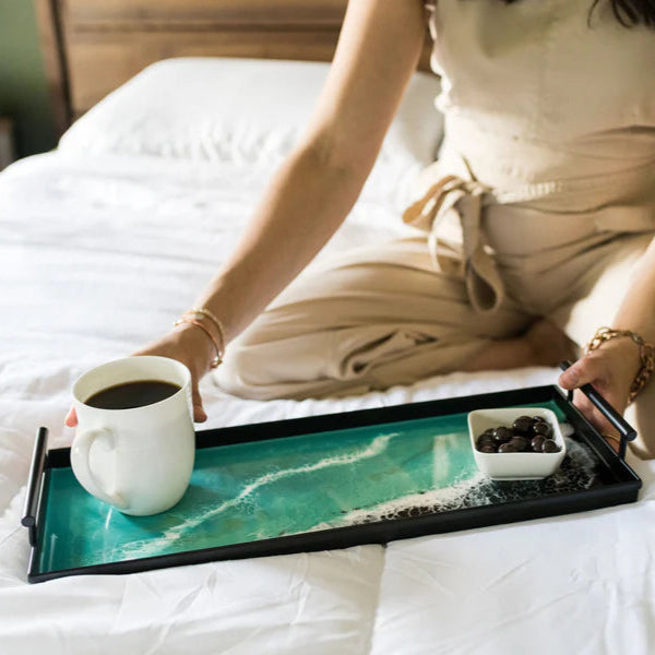 Person sitting on a bed with a resin tray holding a cup of coffee and a small plate.