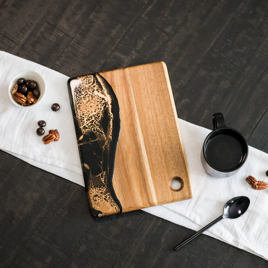 Wooden Cheese Charcuterie Serving Board with black and gold design on a dark surface with a white towel.
