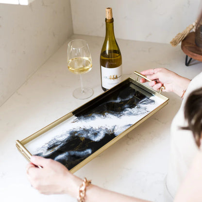 Person holding a decorative resin tray with a bottle of wine and a glass on a kitchen counter.