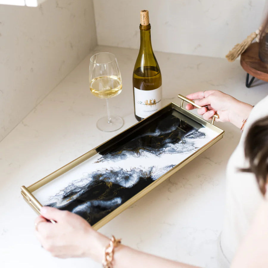 Person holding a decorative resin tray with a bottle of wine and a glass on a kitchen counter.