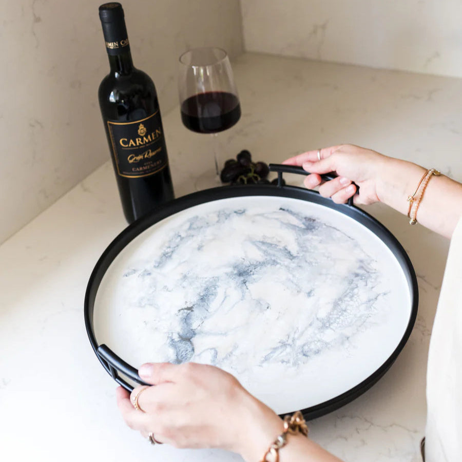 Person holding a marble-patterned resin tray with a bottle of wine and glass in the background.
