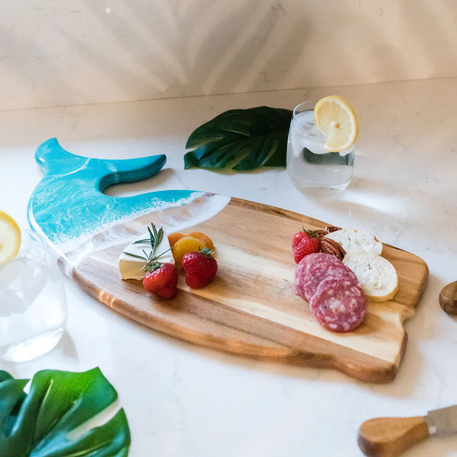 Wooden whale shaped charcuterie board with fruits, vegetables, and a lemon on a white surface.