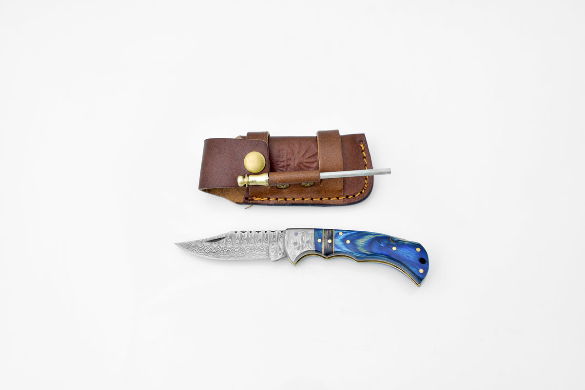 TF-049 Damascus steel Bolster folding knife with leather sheath and belt clip resting on wooden surface