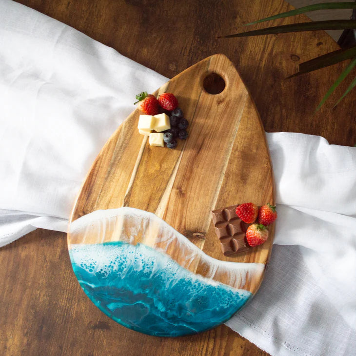 Wooden serving tray with a blue resin design, placed on a wooden surface with a white cloth underneath.
