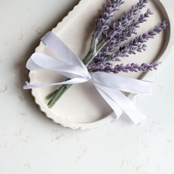 White soap bar with a white ribbon and lavender flowers on a light surface