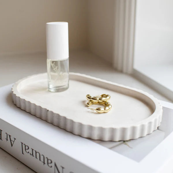 Small white ceramic tray with a gold ring and clear bottle on a book