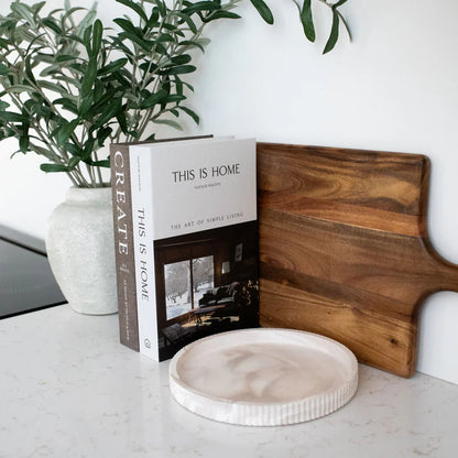 Open book titled 'This is Home' on a marble surface with a wooden cutting board and plant.