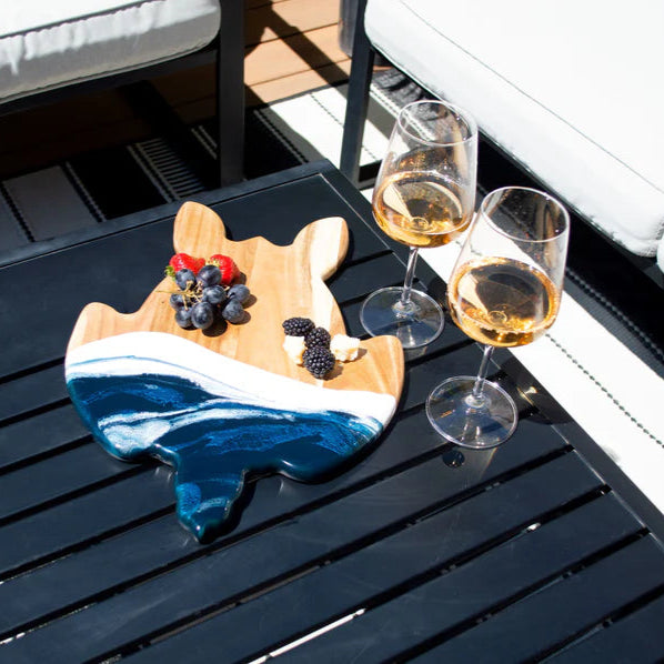 Wine glasses with a small appetizer platter on a wooden resin charcuterie board outdoors.