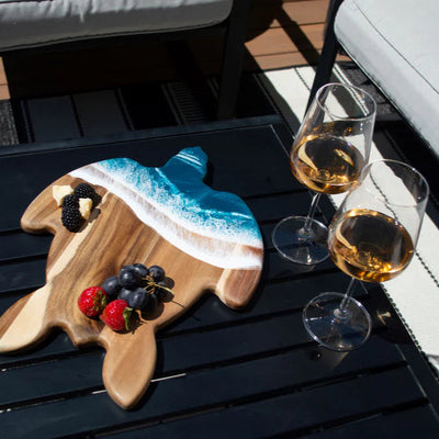 Handcrafted sea turtle-shaped charcuterie board with acacia wood and blue resin accents, topped with fruit and cheese.
