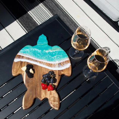 Handcrafted sea turtle-shaped charcuterie board with acacia wood and blue resin accents, topped with fruit and cheese.
