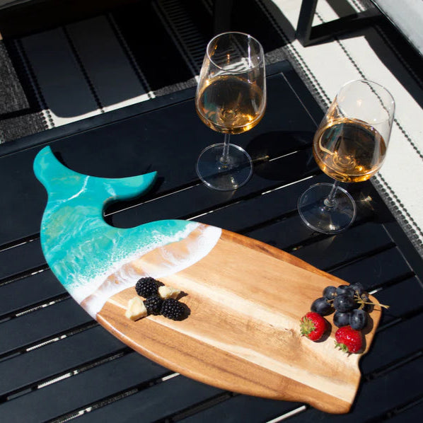Wooden whale shaped charcuterie board with berries and a whale design on a black table outdoors.