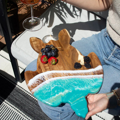 Handcrafted sea turtle-shaped charcuterie board with acacia wood and blue resin accents, topped with fruit and cheese.