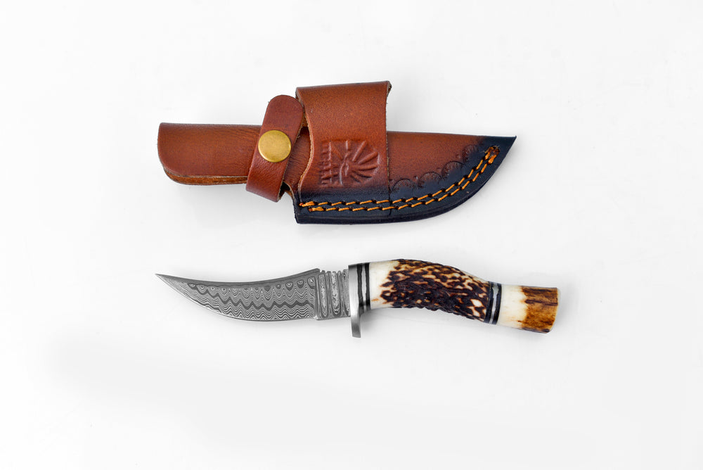 Deer Horn Trailblazer Damascus knife with stag horn handle and leather sheath on wood surface