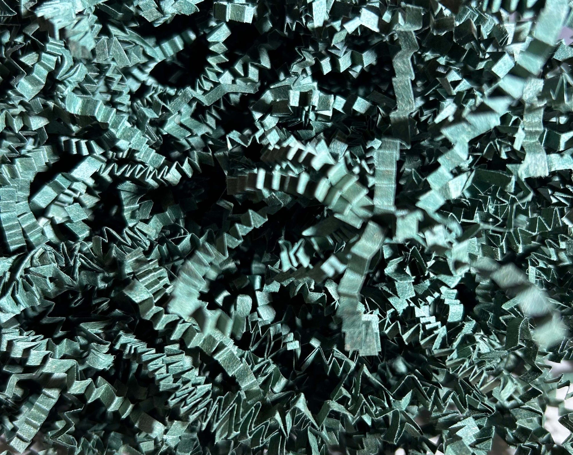 Dark green crinkle paper shredded packing material scattered on a white surface