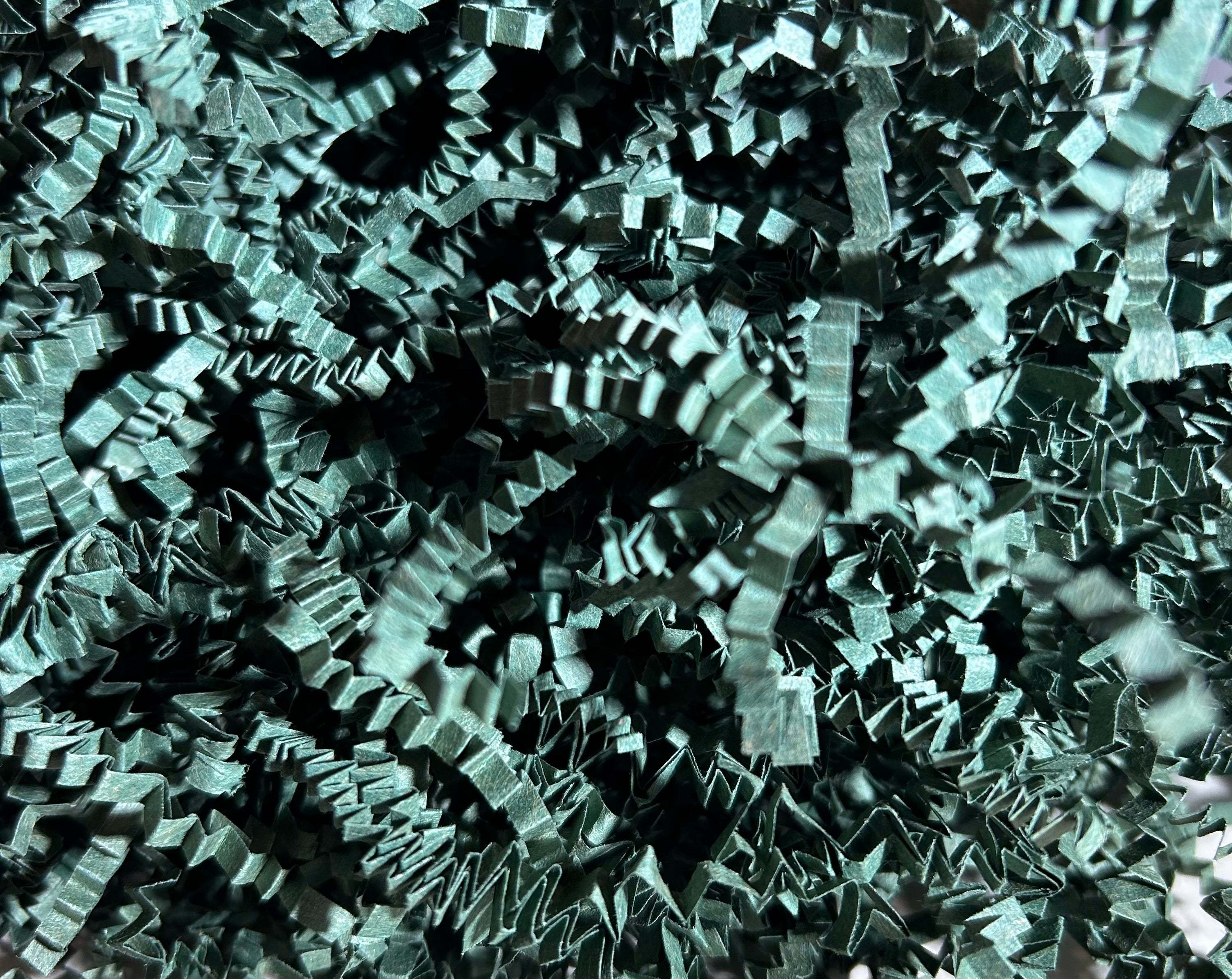 Dark green crinkle paper shredded packing material scattered on a white surface