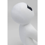 Abstract white figurine with a smooth, rounded head and a single large black patch over one eye, shown against a plain background.