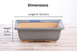 Square bonsai pot with a blue glazed rim fading into gray sides and a natural clay interior, measuring 8 inches long and 2.75 inches high, shown from the side on a wooden surface.