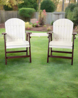 Pair of outdoor chairs with white slatted curved backs and seats, dark brown armrests and legs, placed on green grass in a backyard setting.
