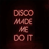 Vertical pink neon sign on black background reading 'DISCO MADE ME DO IT' in a simple sans-serif style.