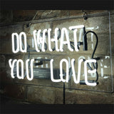 White neon sign reading 'DO WHAT YOU LOVE' mounted on a transparent panel against a rough stone wall, with visible wiring and power supply beneath the text.