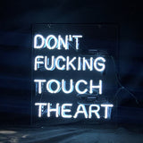 White neon sign on a clear backing reading 'DON'T FUCKING TOUCH THE ART' against a dark background with visible wiring and transformers