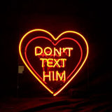 Glowing neon sign in a heart shape with the words "DON'T TEXT HIM" in bright red and orange-yellow colors against a dark background.