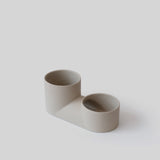 Minimalist double planter with two cylindrical beige vessels of different heights connected by a rectangular base, shown on a neutral background.