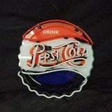 Round Pepsi-Cola neon sign shaped like a bottle cap with red, white, and blue sections and scripted 'Pepsi-Cola' lettering on a black background.