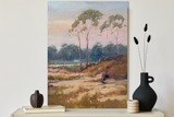 Canvas print titled Dune Sentinels depicting three tall trees on a sandy grassy dune with a cloudy sky, leaning on a white wall above a shelf with vases and books.