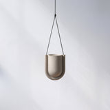 Minimalist beige ceramic planter with a smooth U-shaped curve, suspended by a thin black cord against a plain light gray background.