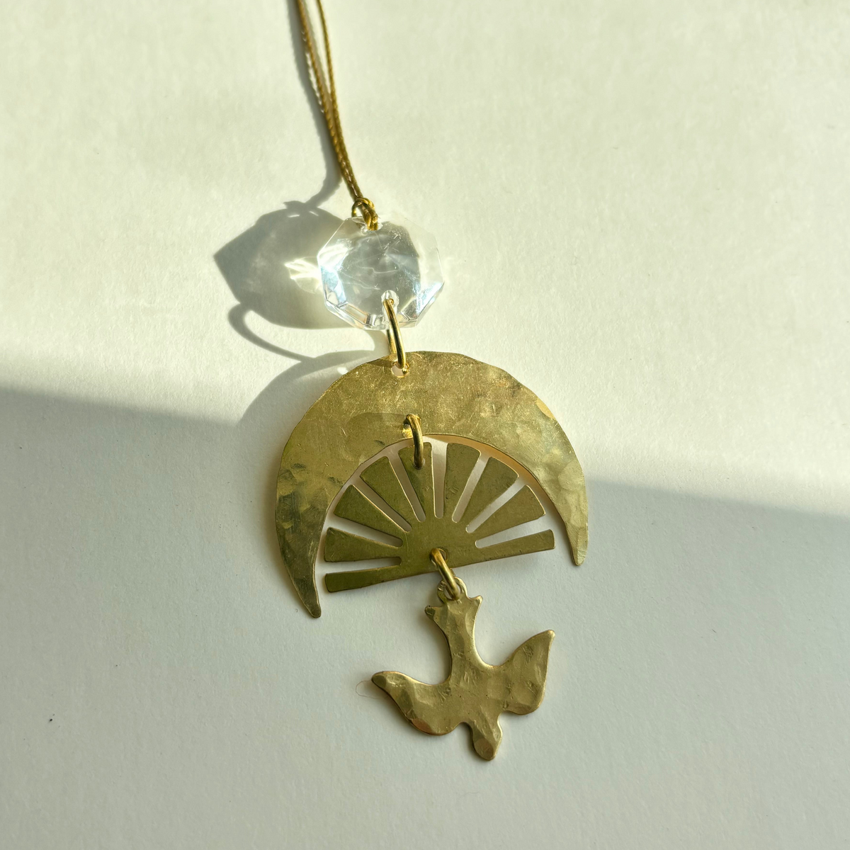 Chasing Light Ornament with hand-cut brass and vintage glass crystal hanging against white background
