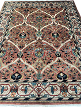 Hand-knotted wool rug with intricate floral and vine motifs in red, blue, black, and beige, featuring a patterned border with geometric and floral elements.