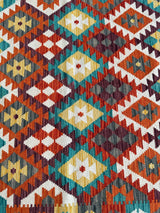 Close-up of Afghani Maimana Kilim rug featuring a repeating diamond pattern in red, mustard yellow, teal, white, and brown tones woven in wool.