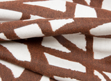 Close-up of rust-colored fabric with an abstract white geometric pattern, showing textured weave and softly folded surface details.