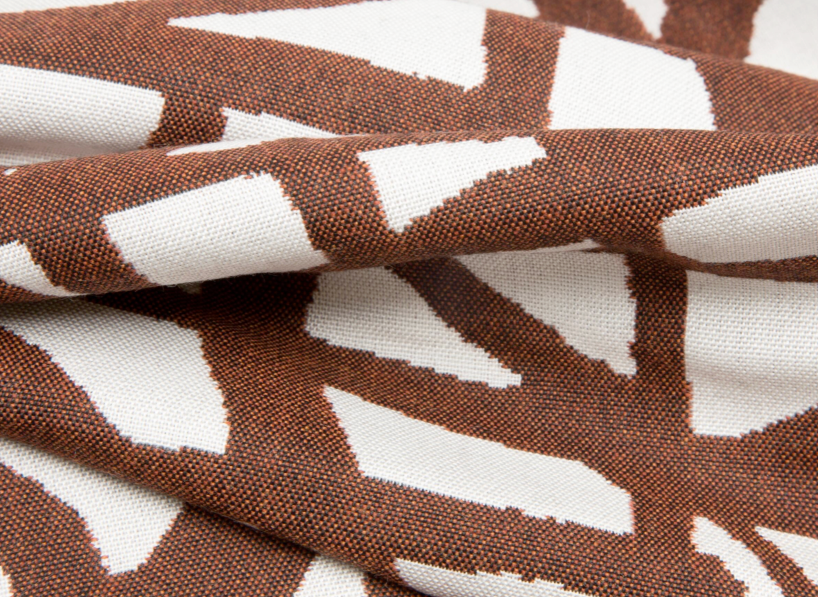 Close-up of rust-colored fabric with an abstract white geometric pattern, showing textured weave and softly folded surface details.