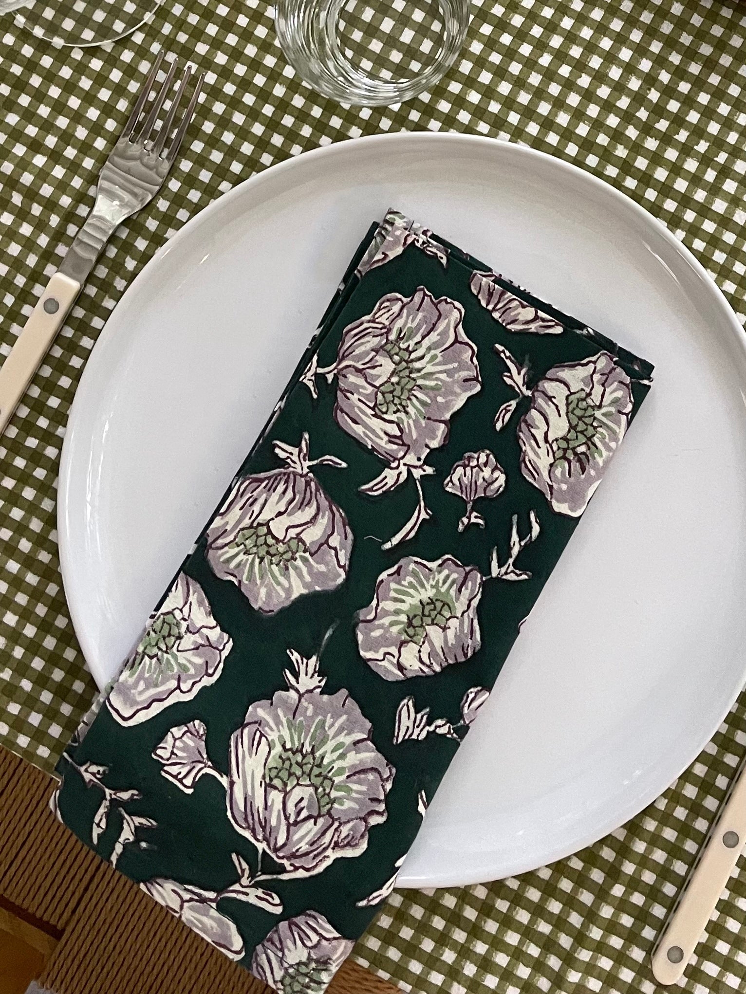 Set of six emerald wild poppy floral cloth napkins stacked on an olive green tablecloth